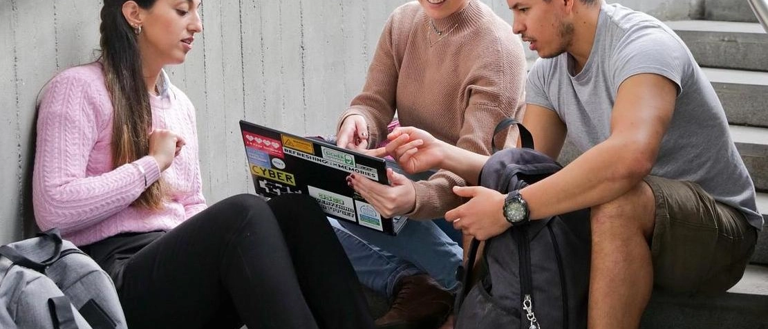 Drei junge Leute sitzen auf einer Treppe und schauen auf einen Laptop.