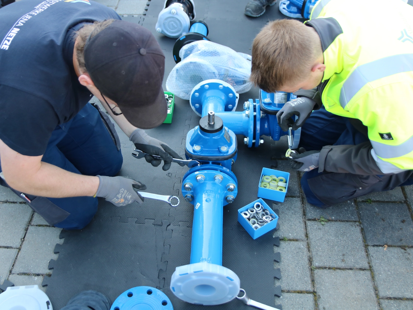 Mitarbeitende der Stadtwerke Jena Netze schrauben große blaue Trinkwasserrohre zusammen