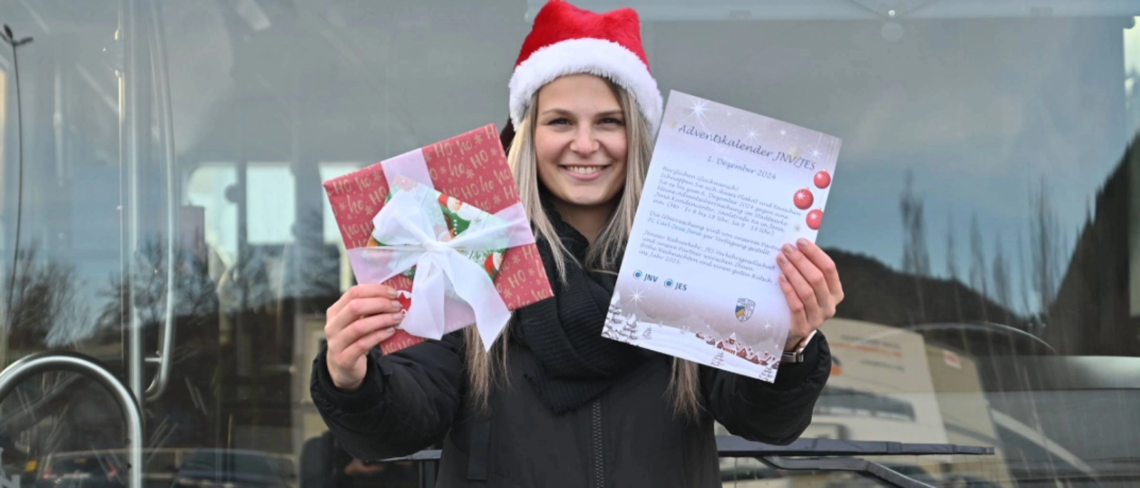 Eine Mitarbeiterin des Jenaer Nahverkehrs vor einem Bus, in den Händen hält sie ein Geschenk und ein Plakat zur Aktion. 